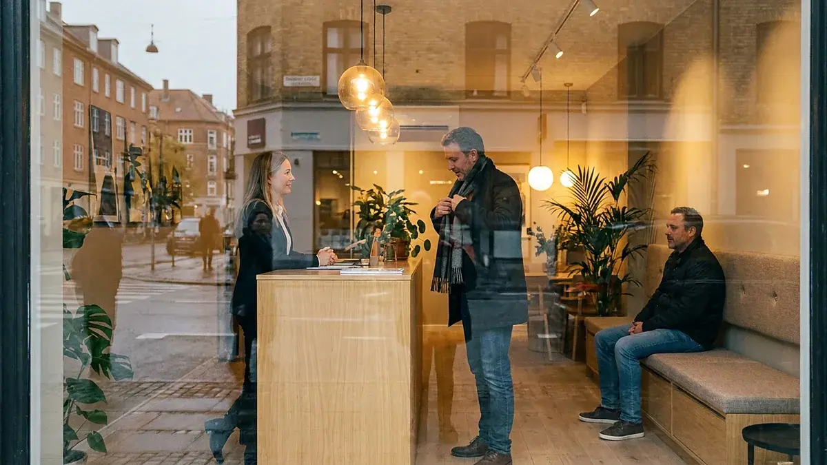 Client accueilli au comptoir d'une agence immobilière, vu à travers la vitrine